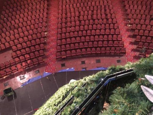 View from above of a theater stage with empty red seats arranged in a semicircle and scattered confetti on the floor.