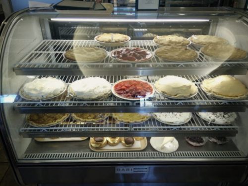 A display case filled with various pies, including fruit and cream varieties, arranged on shelves.