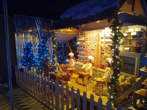 A festive display featuring decorated trees, lights, and figurines in a cozy, winter-themed setting.