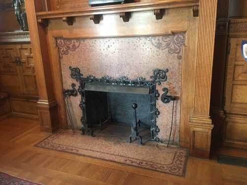 A decorative fireplace with an ornate metal screen and wooden paneling, set in a classic interior.