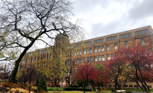 A brick building surrounded by trees with autumn foliage under a cloudy sky.