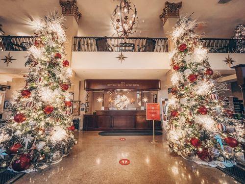 Two festive Christmas trees adorned with red ornaments and lights flank a hotel lobby decorated for the holidays.