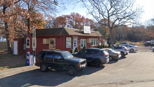 A red diner with a sign, surrounded by parked cars and autumn trees in the background.