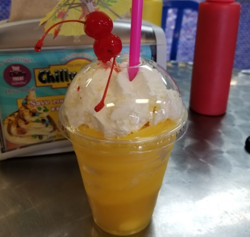 A colorful drink topped with whipped cream, cherries, and a small umbrella, served in a clear cup.