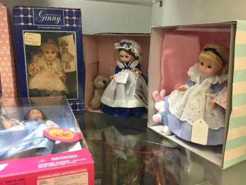 A display of vintage dolls in their boxes, featuring various outfits and accessories, including a teddy bear.