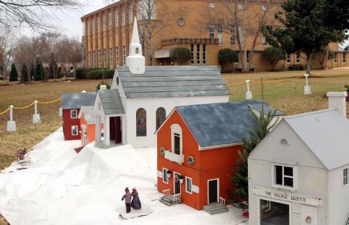 A miniature village scene with colorful houses and a church, set on a snowy landscape near a school building.