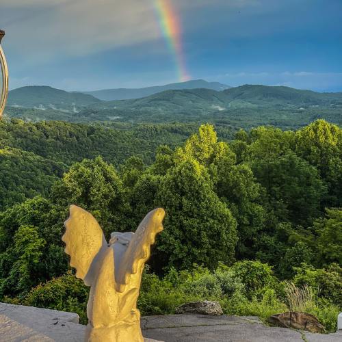 A scenic view of rolling green hills under a rainbow, with a stone angel statue in the foreground.
