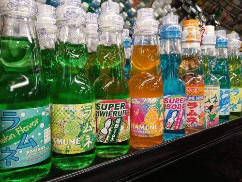A colorful display of various Ramune soda bottles in different flavors, including melon and orange, on a store shelf.