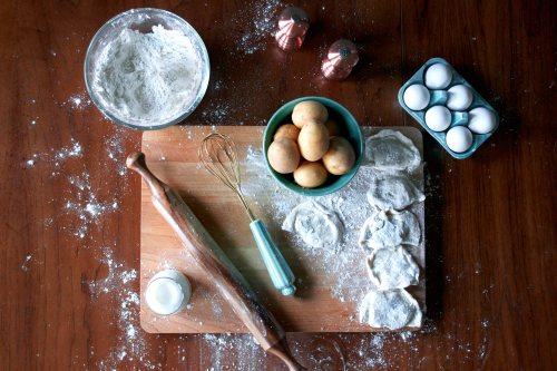 A wooden countertop with flour, eggs, a rolling pin, and dough pieces, surrounded by baking ingredients.