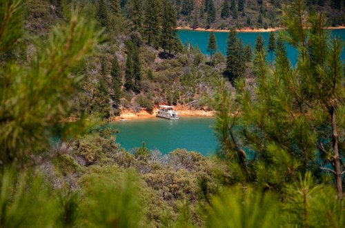 A boat anchored near a lush, green shoreline by a tranquil blue lake, surrounded by trees and hills.