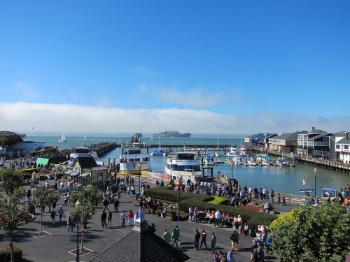 A bustling harbor scene with boats, people, and clear blue skies, showcasing a lively waterfront atmosphere.
