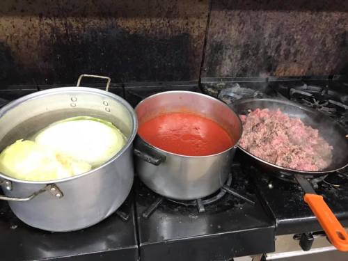 Three pots on a stove: one with boiling cabbage, one with tomato sauce, and one with cooked ground meat.