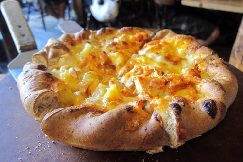 A freshly baked pizza with a golden crust, topped with cheese and pineapple, sitting on a wooden surface.
