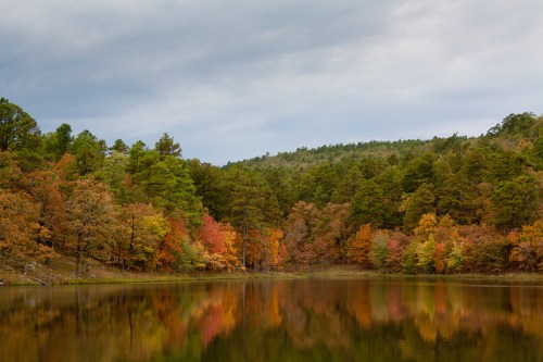 A serene lake surrounded by trees displaying vibrant autumn colors under a cloudy sky.