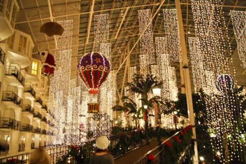 A festive indoor scene with hanging lights, hot air balloons, and holiday decorations in a beautifully lit atrium.
