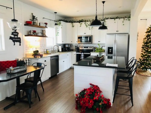 Bright kitchen with white cabinets, black appliances, and festive decor, featuring a dining table and a Christmas tree.