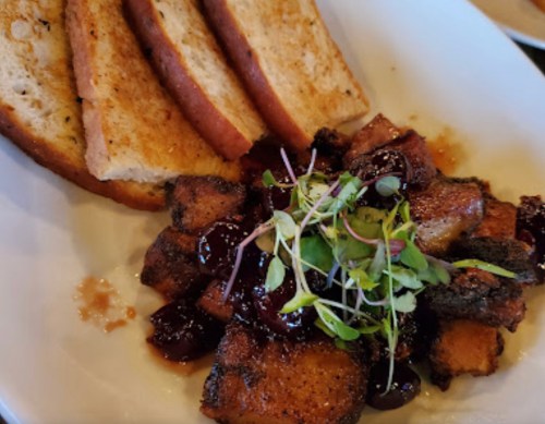 A plate featuring crispy fried tofu with a dark sauce, garnished with microgreens, alongside slices of toasted bread.