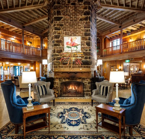 Cozy lodge interior featuring a stone fireplace, armchairs, and warm wooden decor, creating a welcoming atmosphere.