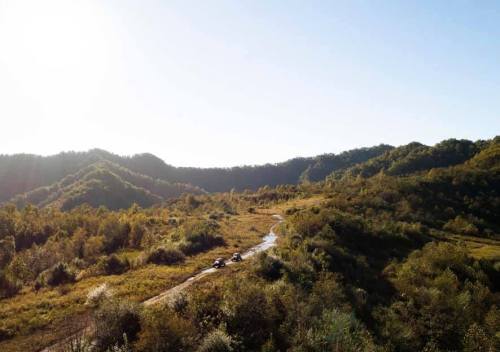 Aerial view of a winding dirt path through lush green hills under a clear blue sky.