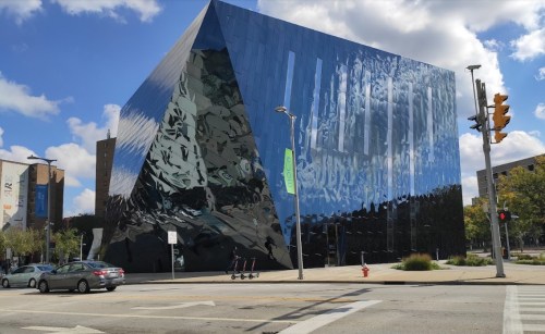 A modern, angular building with a reflective glass facade under a blue sky with clouds.