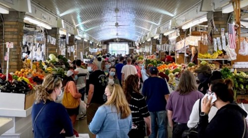 A bustling market filled with people shopping for fresh produce and goods, with colorful fruits and vegetables on display.