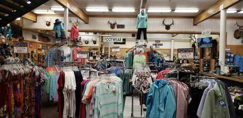 A retail store interior filled with clothing racks, footwear signs, and mounted animal heads on the walls.