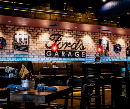 Interior of a restaurant with a brick wall, vintage photos, and a sign reading "Trol's Garage." Tables and chairs are set.