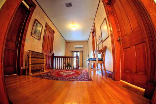 A hallway with wooden doors, a chair, and a patterned rug, featuring warm lighting and vintage decor.