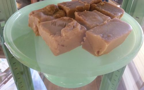 A green glass pedestal displays several pieces of creamy fudge, showcasing a smooth texture and light brown color.