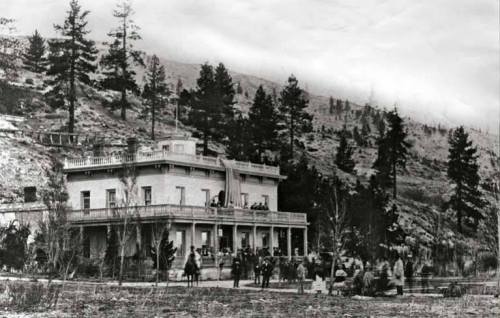 Historic black-and-white photo of a large building surrounded by trees, with people gathered outside.