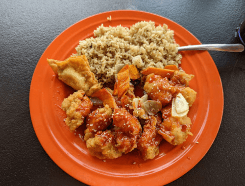 A vibrant orange plate with sweet and sour chicken, fried rice, and a crispy wonton.