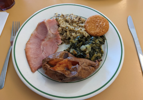 A plate with ham, rice, cornbread, collard greens, and a baked sweet potato.