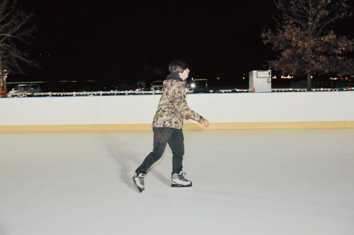 A person skating on an outdoor ice rink at night, wearing a camouflage jacket and black pants.