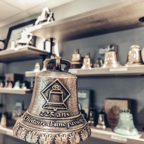 A decorative bell with a crown emblem, displayed in front of a shelf filled with various other bells.