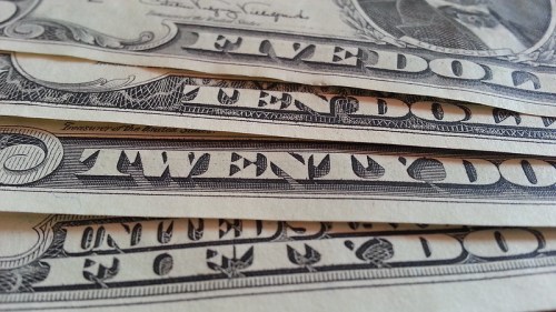 Close-up of U.S. currency, featuring a five-dollar bill and a twenty-dollar bill stacked together.