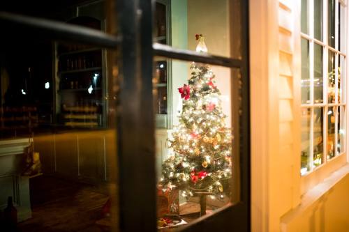 A beautifully decorated Christmas tree with lights and ornaments, seen through a window at night.
