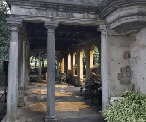 A stone pavilion with columns and arches, illuminated softly by warm light, surrounded by greenery.