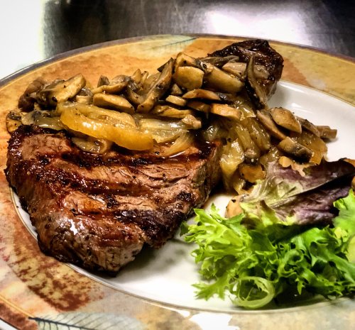 A plate featuring a grilled steak topped with sautéed mushrooms and onions, accompanied by a side of mixed greens.