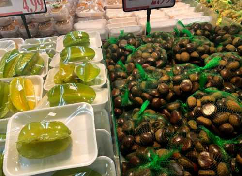 Fresh green produce in trays, including starfruit and chestnuts, displayed in a market setting.