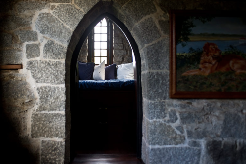 A stone archway leads to a cozy nook with cushions, beside a framed painting of a lion on the wall.
