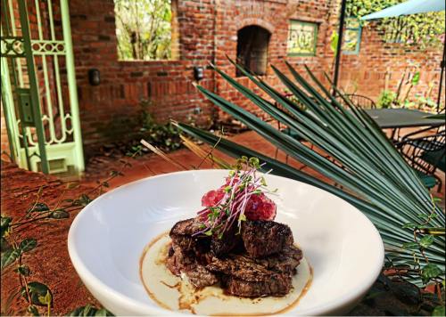 A beautifully plated steak dish garnished with microgreens and sauce, set against a rustic outdoor backdrop.