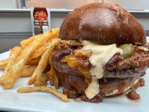 A hearty burger with melted cheese, toppings, and fries on a plate, with a bottle of ketchup in the background.