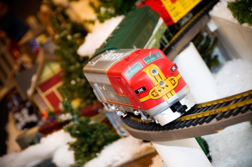 A red toy train on a circular track, surrounded by miniature trees and festive decorations.