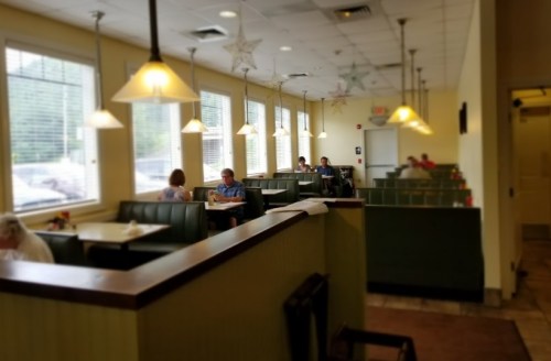 A cozy diner interior with green booths, large windows, and soft lighting, featuring a few patrons dining.