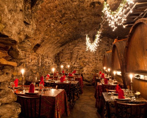 Cozy underground restaurant with stone walls, candlelit tables, and festive decorations.