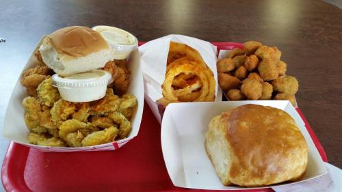 A red tray with fried shrimp, hush puppies, curly fries, and a biscuit, accompanied by dipping sauces.
