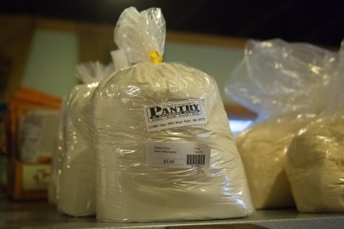 A bag of all-purpose flour labeled with a price tag, sitting on a shelf in a pantry store.