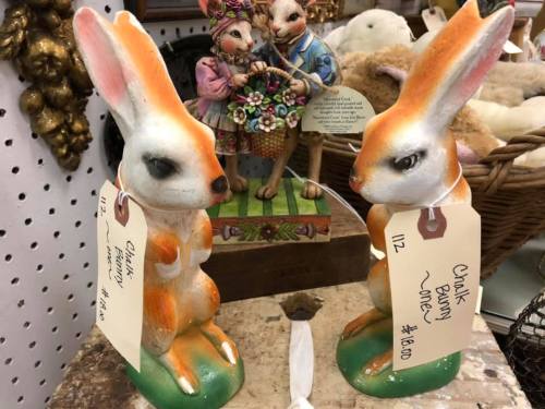 Two decorative ceramic bunnies with orange accents, labeled for sale, beside a figurine of two rabbits in a basket.
