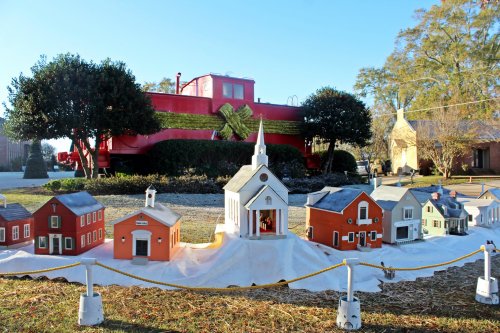 A miniature village with colorful houses and a church, set in front of a red train car and greenery.