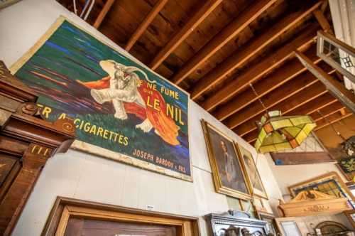 A vintage shop interior featuring a colorful poster, framed art, and a stained glass lamp under a wooden ceiling.